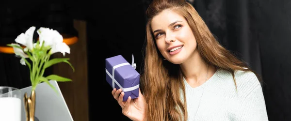 Beautiful smiling woman thinking and holding gift box in cafe — Stock Photo