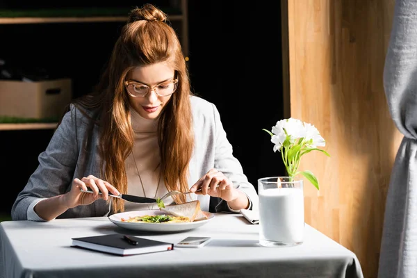 Attractive woman eating breakfast in cafe with notepad and smartphone — Stock Photo