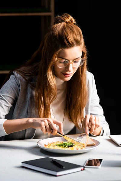 Redhead woman eating breakfast in cafe with notepad and smartphone — Stock Photo