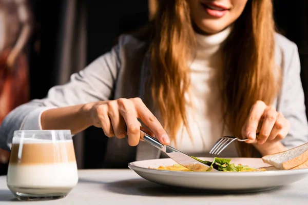 Cropped view of woman eating breakfast with glass of coffee in cafe — Stock Photo
