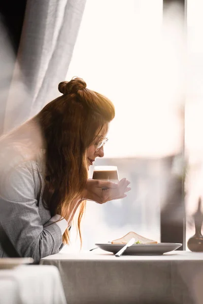 Donna felice avendo caffè e prima colazione in caffè vicino alla finestra — Foto stock