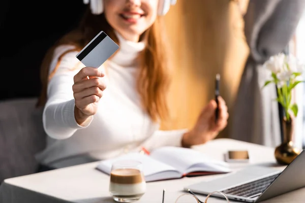 Vista cortada de mulher em fones de ouvido pagando com cartão de crédito no café, foco seletivo — Fotografia de Stock