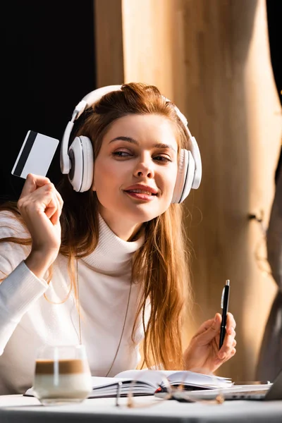 Attractive redhead woman in headphones paying with credit card in cafe — Stock Photo