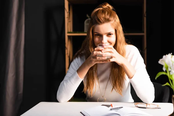 Mulher feliz atraente segurando vidro de café no café com bloco de notas — Fotografia de Stock