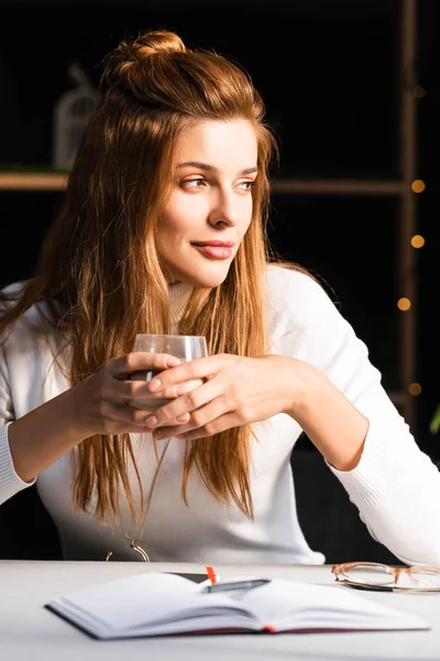 Beautiful pensive woman holding glass of coffee in cafe with notepad — Stock Photo