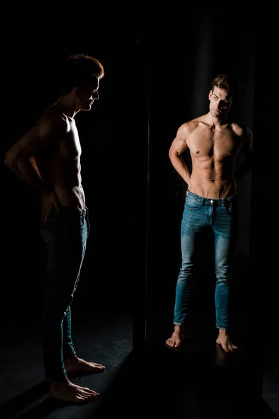 Schöner Mann ohne Hemd posiert im dunklen Raum vor dem Spiegel — Stockfoto