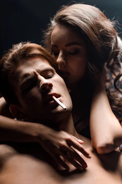 Bella ragazza abbracciare seducente fidanzato fumare sigaretta, isolato su nero — Foto stock