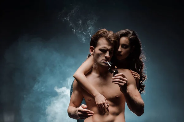 Sexy mujer abrazo hombre fumar cigarrillo en oscuro habitación con humo - foto de stock