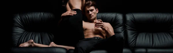 Сексуальная женщина и мужчина со стаканом виски позируют на диване в темной комнате — стоковое фото