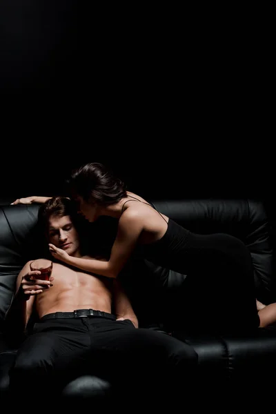 Passionate woman and man with glass of whiskey posing on sofa in dark room — Stock Photo