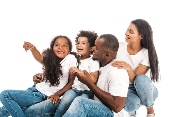 Sorridente bambino afro-americano che distoglie lo sguardo e punta il dito mentre siede vicino ai genitori e al fratello isolato sul bianco — Foto stock