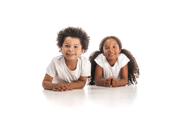 Щасливий афроамериканський брат і сестра посміхаються на камеру, лежачи на білому тлі — стокове фото