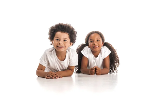 Happy african american brother and sister smiling at camera while lying on white background — Stock Photo