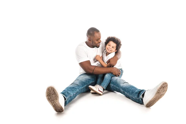 Heureux afro-américain homme étreignant fils mignon tout en étant assis sur fond blanc — Photo de stock