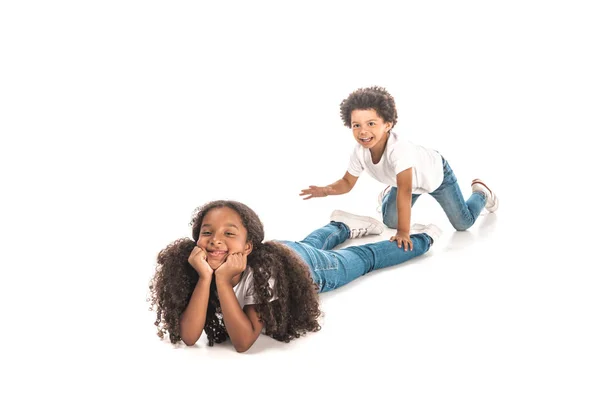 Fröhliche afrikanisch-amerikanische Junge schleichen bis zu liegender Schwester auf weißem Hintergrund — Stockfoto