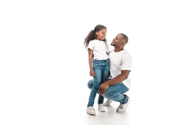 Feliz afro-americano padre en cuclillas y hablando con adorable hija sobre fondo blanco - foto de stock