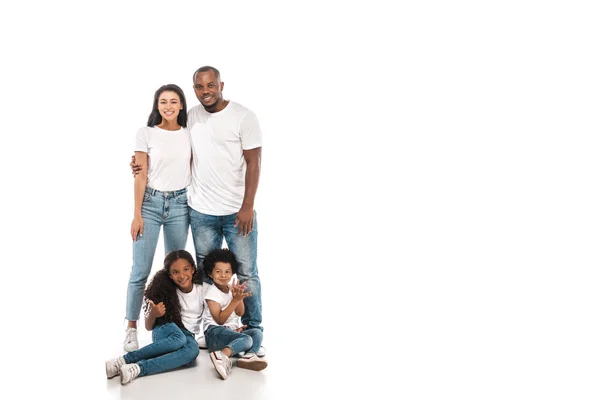 Lächelnder afrikanisch-amerikanischer Mann umarmt Frau, während er neben Kindern steht, die auf weißem Hintergrund sitzen — Stockfoto