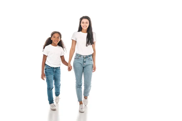 Happy african american mother and daughter holding hands and looking at camera while walking on white background — Stock Photo