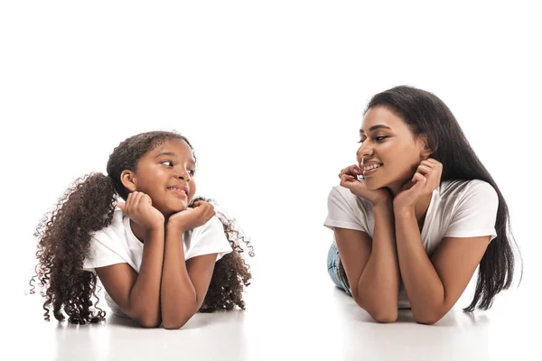 Happy african american mother and daughter looking at each other while lying ion white background — Stock Photo