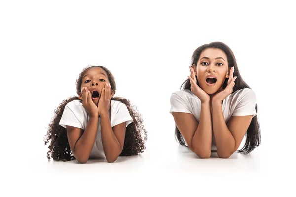 Shocked african american mother and daughter looking at camera while lying on white background — Stock Photo