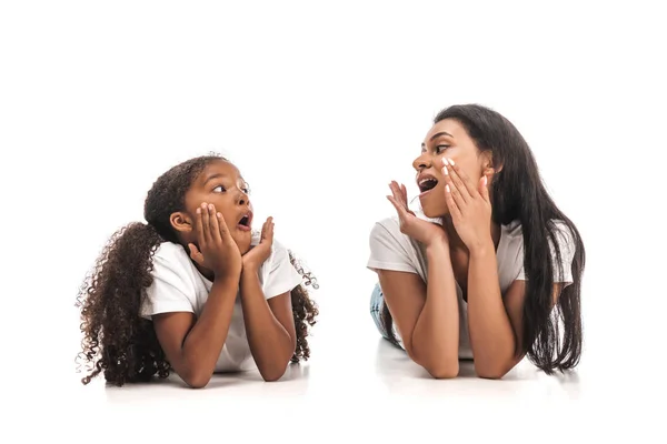 Shocked african american mother and daughter looking at each other while lying on white background — Stock Photo