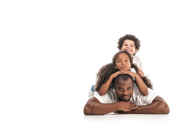 Africano americano hija y hijo tener divertido mientras acostado en padres espalda juntos en blanco fondo - foto de stock