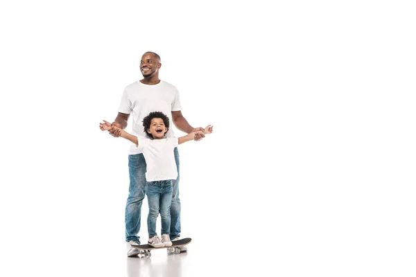 Feliz afro-americano homem de apoio alegre filho de pé no penny board no fundo branco — Fotografia de Stock