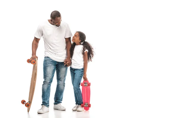 Schöner afrikanisch-amerikanischer Mann mit Longboard schaut entzückende Tochter an, die Schlittschuh auf weißem Hintergrund hält — Stockfoto