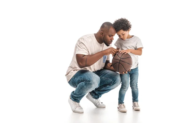 Africano americano hombre mostrando baloncesto a adorable hijo en blanco fondo - foto de stock