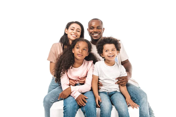 Feliz africano americano esposa y marido abrazando adorable hijos mientras sentado aislado en blanco - foto de stock