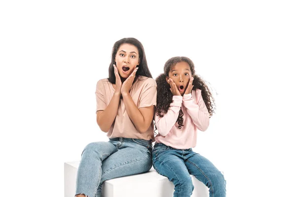 Conmocionó a la madre y la hija afroamericana mirando a la cámara mientras estaban sentadas aisladas en blanco - foto de stock