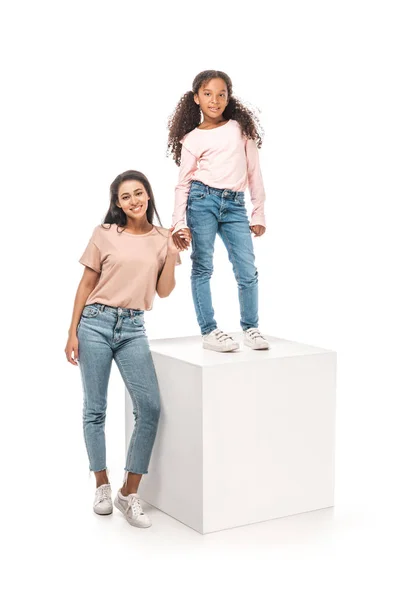 Alegre Africano americano mulher segurando mão de feliz filha de pé no pedestal no fundo branco — Fotografia de Stock