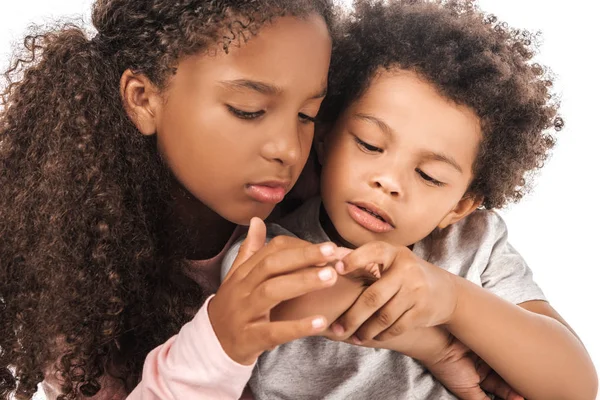 Attentive african american sister looking at hand of adorable brother isolated on white — Stock Photo