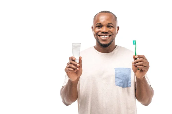 Fröhlicher afrikanisch-amerikanischer Mann hält Zahnbürste und Zahnpasta in der Hand und blickt isoliert in die Kamera — Stockfoto