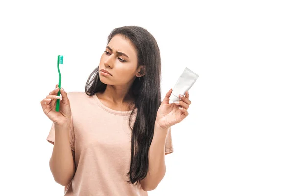 Femme afro-américaine sceptique tenant brosse à dents et dentifrice isolé sur blanc — Photo de stock