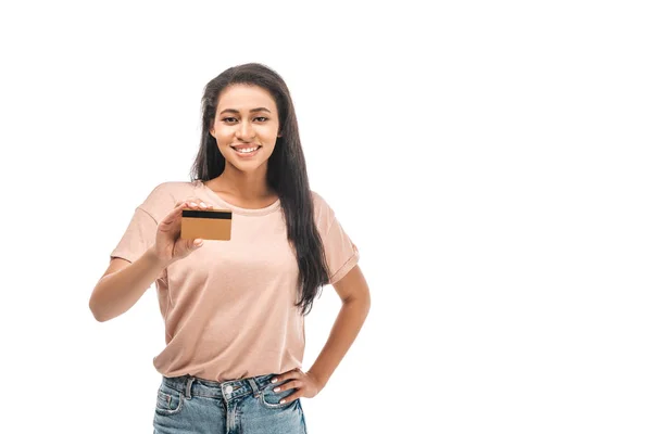 Улыбающаяся африканская американка, стоящая с рукой на бедре и держащая кредитную карту, изолированную на белом — стоковое фото