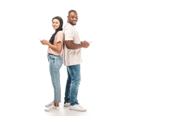 Sourire couple afro-américain debout dos à dos et en utilisant des smartphones sur fond blanc — Photo de stock