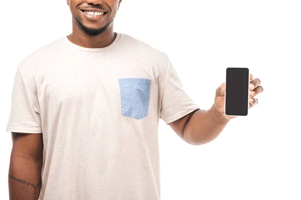 Vista parcial del hombre afroamericano sonriente sosteniendo teléfono inteligente con pantalla en blanco aislado en blanco - foto de stock
