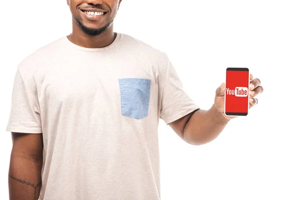 KYIV, UCRAINA - 15 AGOSTO 2019: Vista parziale dell'uomo afro-americano sorridente che tiene smartphone con l'app Youtube sullo schermo isolato su bianco . — Foto stock