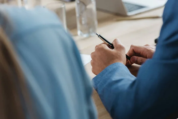 Vista cortada do homem de negócios segurando caneta enquanto sentado na mesa durante a reunião de negócios — Fotografia de Stock