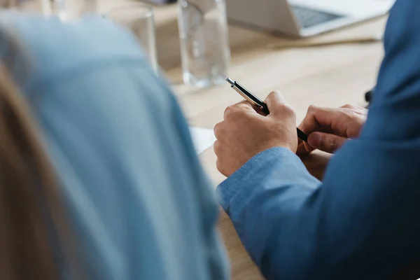 Vista recortada de un hombre de negocios sosteniendo la pluma mientras está sentado en el escritorio durante la reunión de negocios - foto de stock