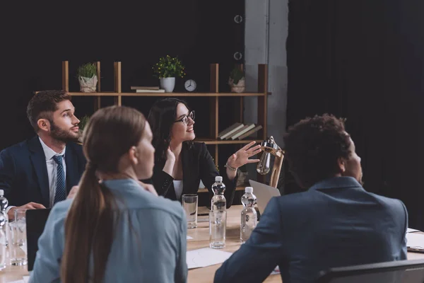 Young businesswoman talking during business meeting while sitting near multicultural colleagues — Stock Photo