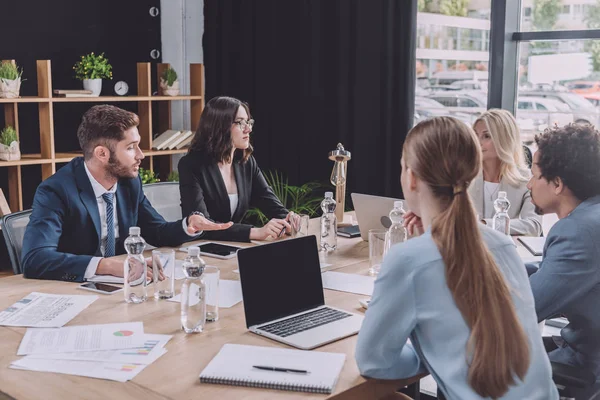 Multicultural colleagues sitting at desk near digital devices and documents during business meeting — Stock Photo