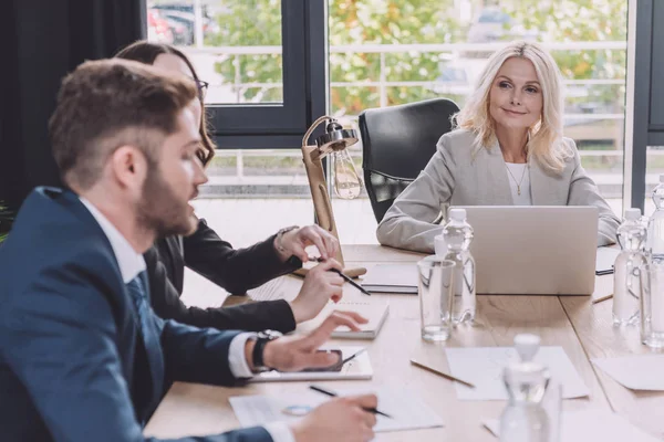 Atenta mujer de negocios mirando joven colega hablando en reunión de negocios - foto de stock