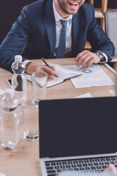 Обрізаний погляд на молодого бізнесмена, який пише в блокноті і сміється на діловій зустрічі — стокове фото