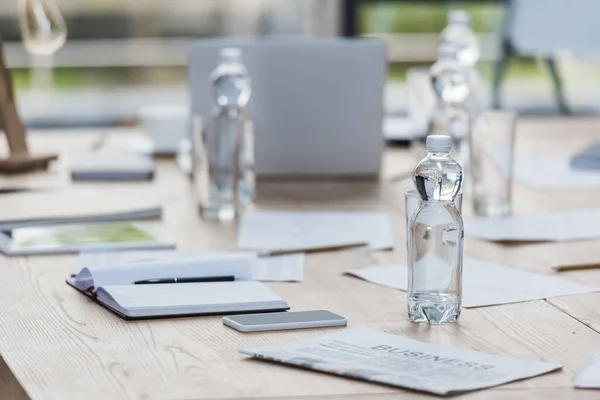 Fuoco selettivo di bottiglia con acqua vicino a smartphone, notebook e documenti su tavolo di legno in sala riunioni — Foto stock