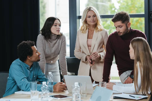 Attractive, mature businesswoman looking at colleague at business meeting with multicultural coworkers — Stock Photo