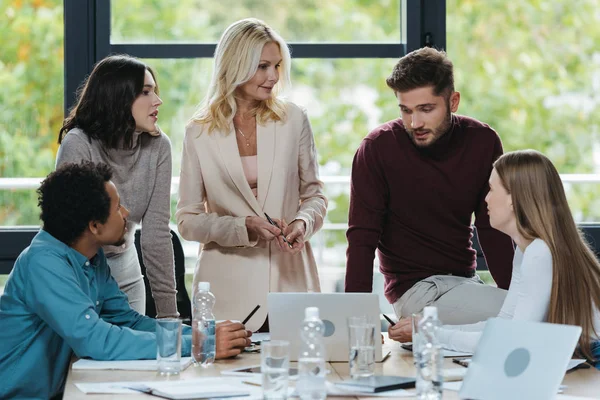 Young multicultural businesspeople talking to mature businesswoman at business meeting — Stock Photo