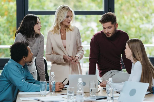 Jóvenes empresarios multiculturales hablando con una mujer de negocios madura en la reunión de negocios - foto de stock