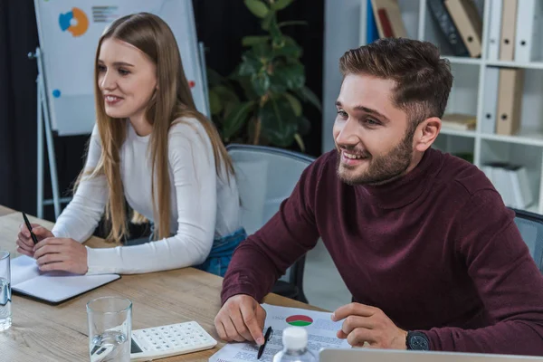 Sonriente hombre de negocios y mujer de negocios sentado en el escritorio en la sala de reuniones - foto de stock